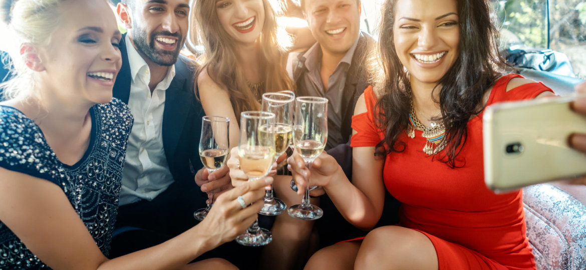 Party people in a limo with drinks taking a selfie with phone smiling into the camera